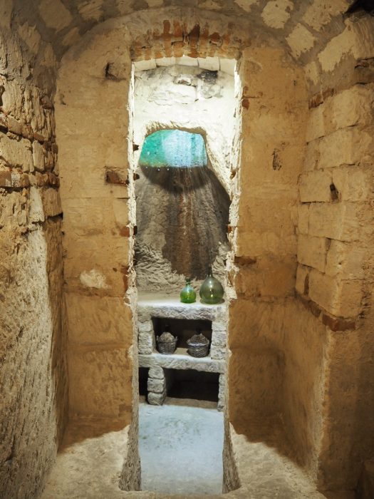 "Interno di un infernot scavato nella Pietra da Cantoni, con volta a botte, pareti in arenaria e bottiglie di vino conservate in nicchie nelle Langhe Roero e Monferrato"