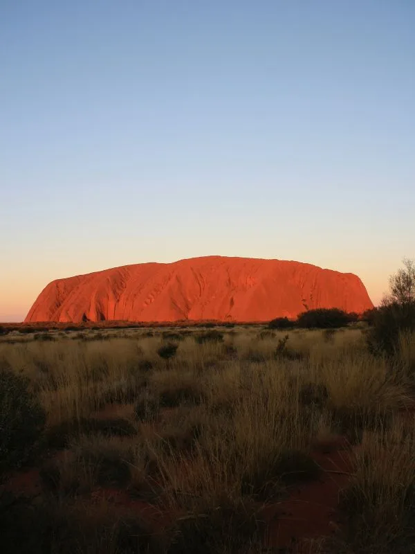 "Paesaggio del deserto rosso australiano con Uluru all’orizzonte, meta affascinante per un viaggio spirituale e naturalistico"